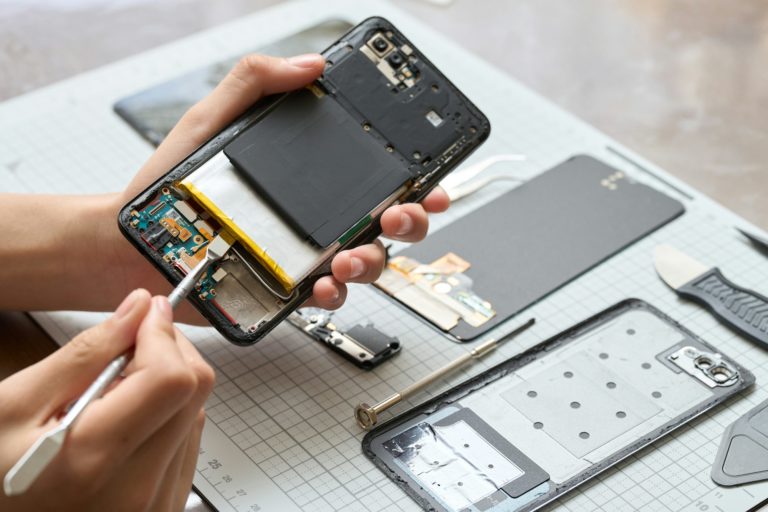 Mains de technicien informatique effectuant la maintenance et le désassemblage d'un smartphone dans un atelier de réparation informatique Teclab