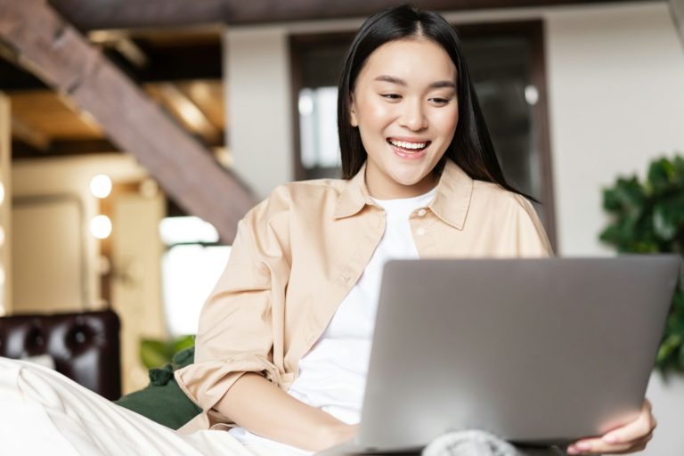 Femme heureuse se reposant chez elle avec un ordinateur portable, achetant des produits informatiques en naviguant sur un site web sur son ordinateur.